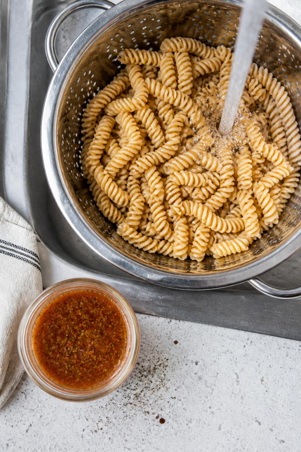 Cooking process, overhead: High-protein rotini just cooked to al dente, being rinsed in a stainless