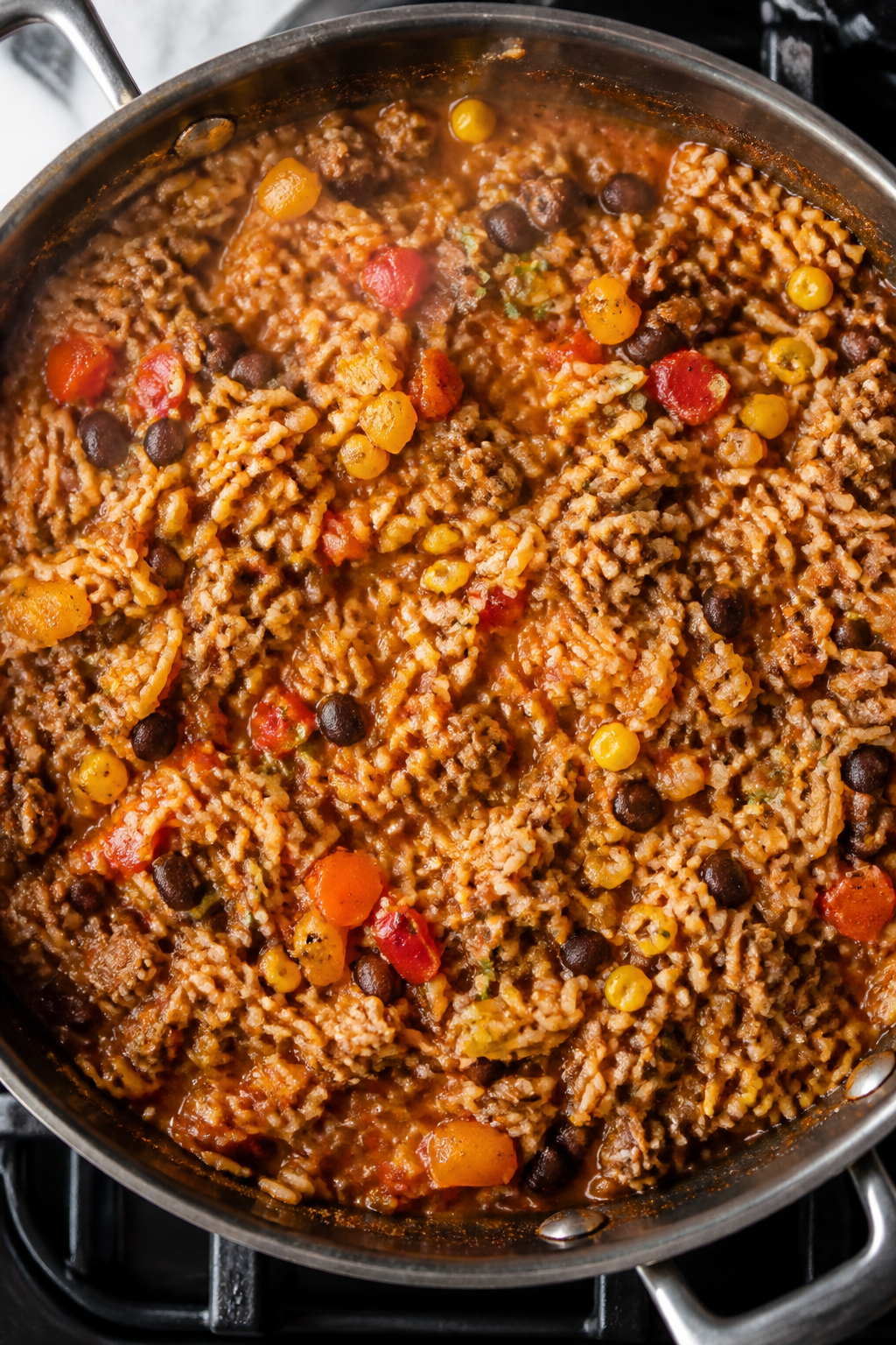 Cooking process, overhead shot: A large, deep skillet on the stovetop with the Mexican rice mixture 