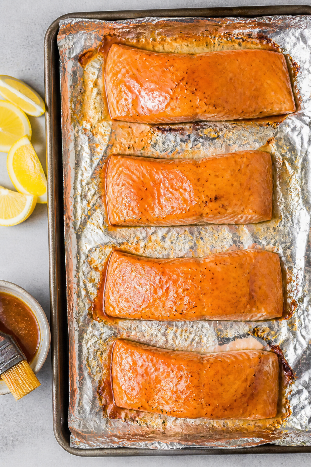 Cooking process: Overhead shot of four salmon fillets on a foil-lined sheet pan mid-recipe—after f