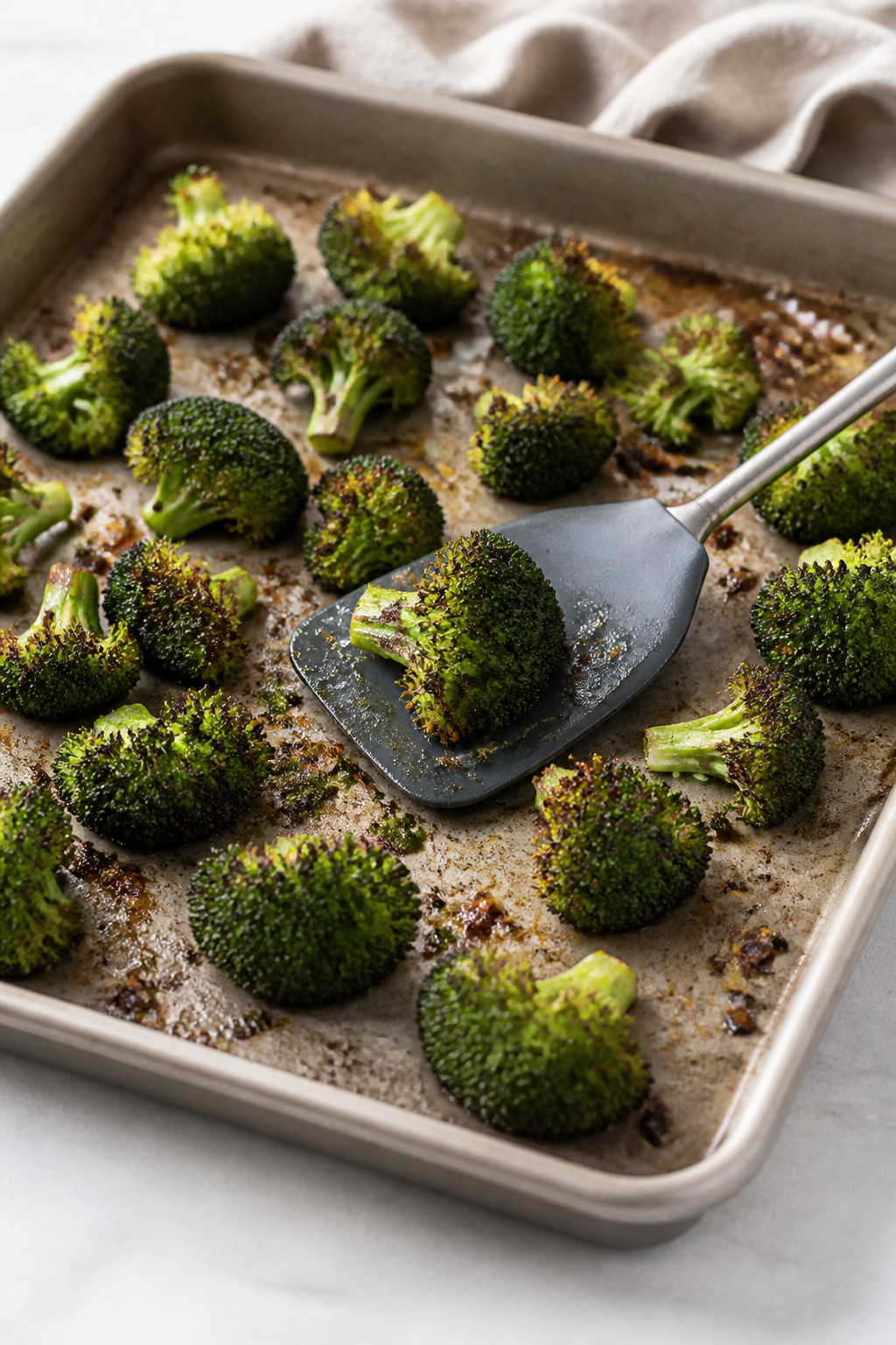 Cooking process: Roasted broccoli just out of the oven on a sheet pan, edges deeply caramelized and 