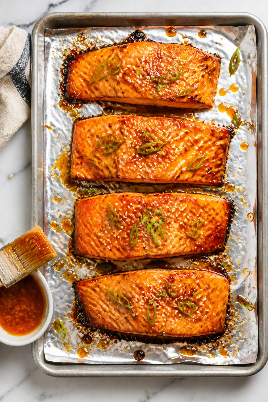 Tasty top view: Overhead shot of four salmon fillets on a foil-lined sheet pan just out of the oven,