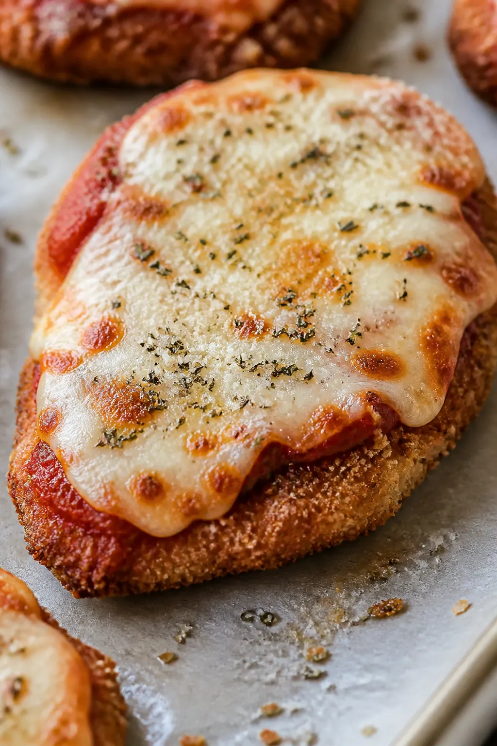 Close-up detail: Oven-baked chicken Parmesan cutlet just out of the oven with melted part-skim mozza