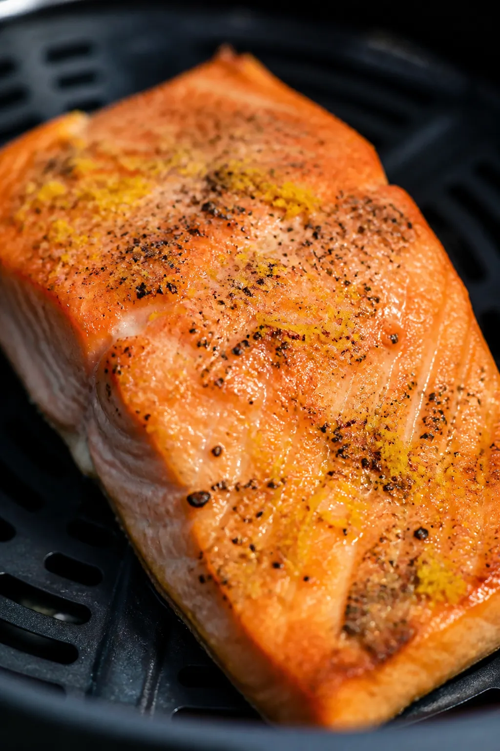 Close-up detail: Tender, flaky air-fried salmon fillet just out of the basket, edges lightly crisp a