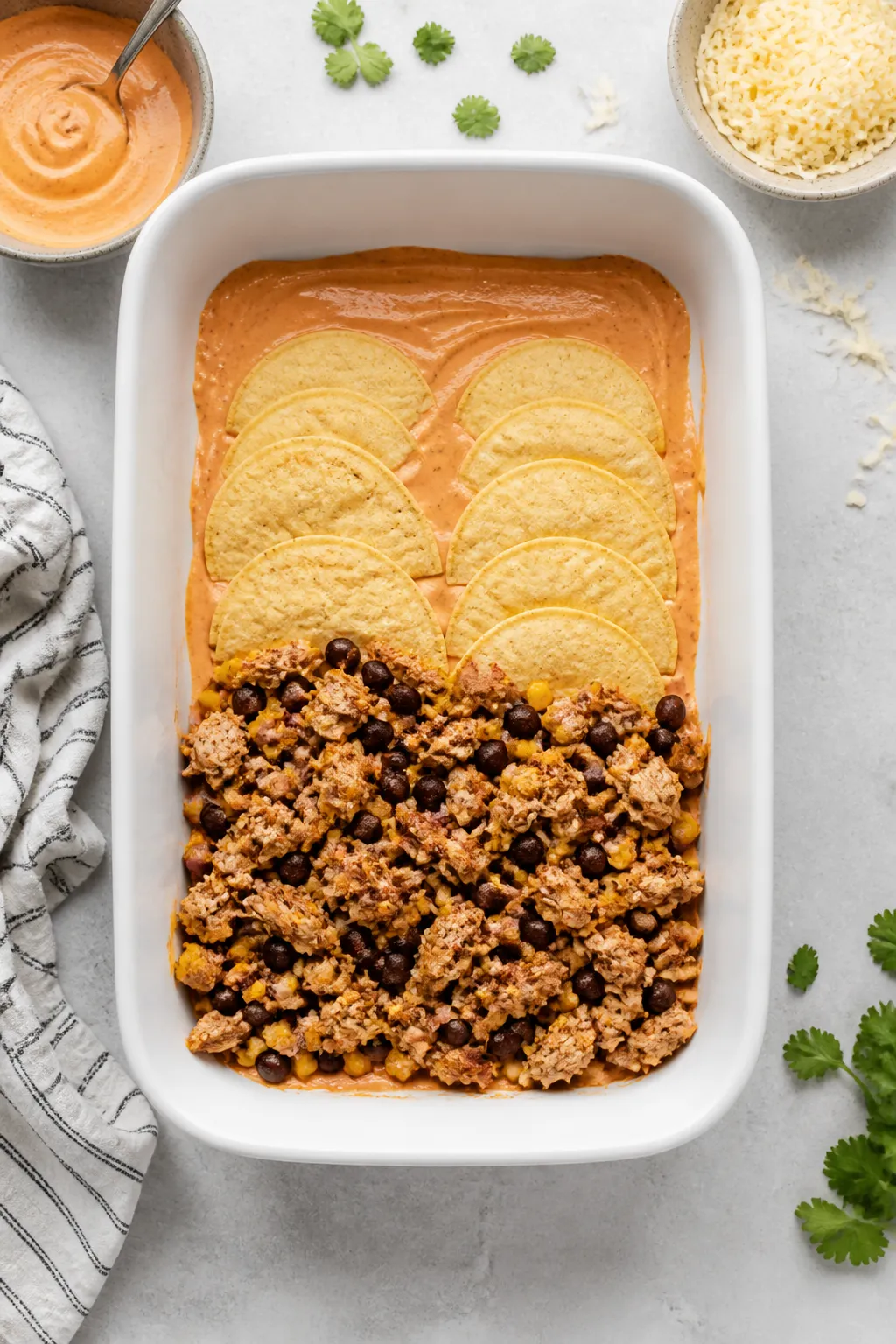 Cooking process: Overhead shot of the layering stage in a 9x13 baking dish—thin smear of creamy re