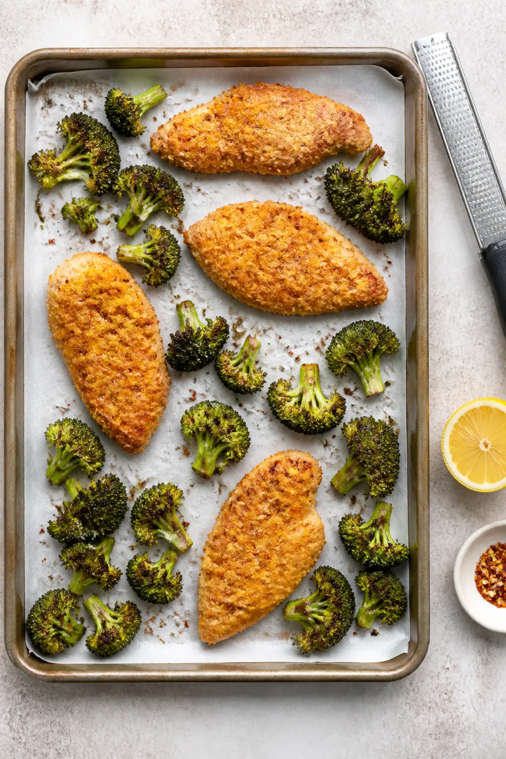 Cooking process: Overhead shot of the sheet pan mid-bake at the flip stage—parmesan-crusted chicke