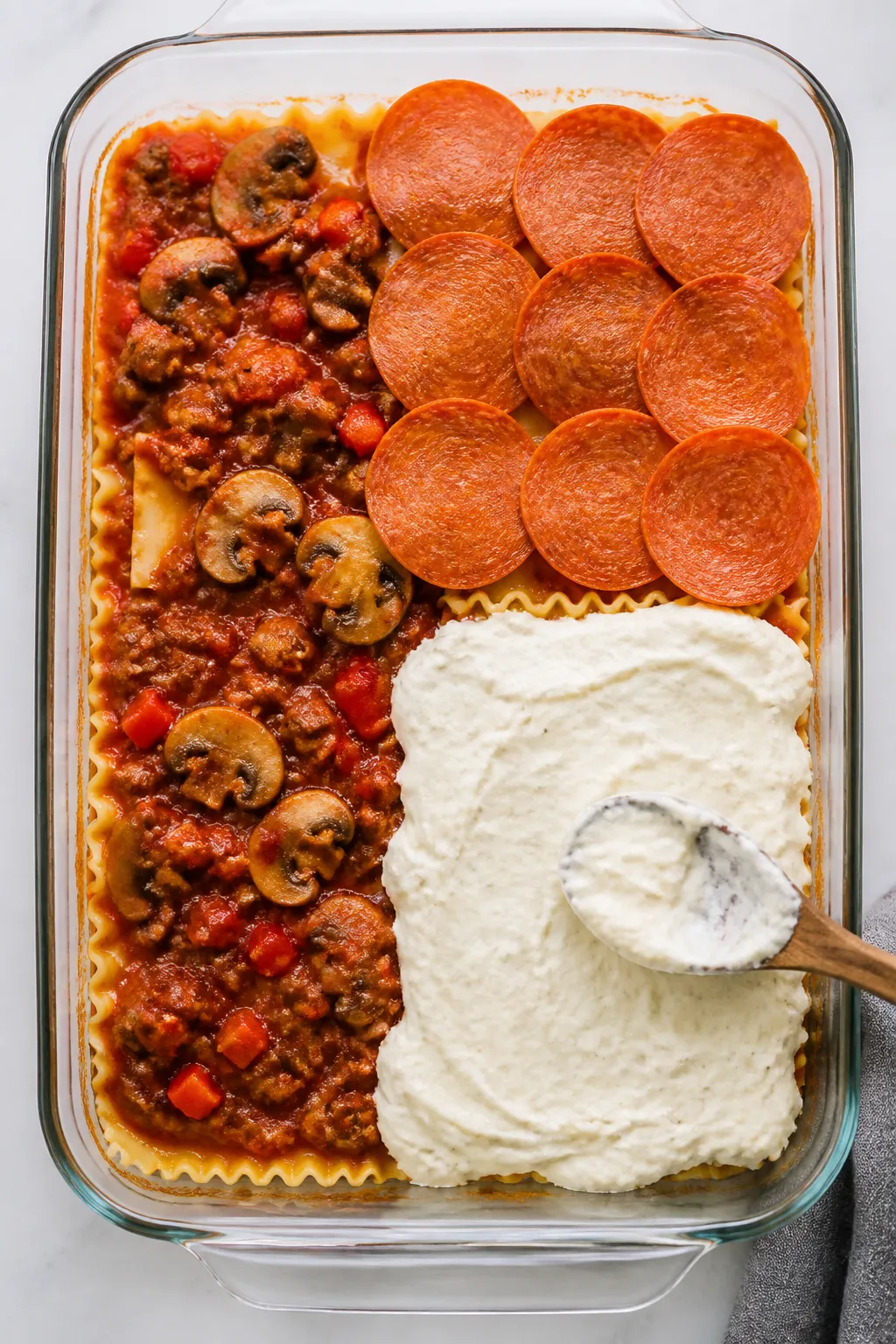 Cooking process shot: Overhead view of assembly in a 9x13 baking dish—half the pasta and meat sauc